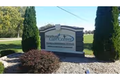 Outdoor view of a stone sign for Freeburg Care Center surrounded by landscaping with bushes and tall evergreen trees, set against a backdrop of a clear sky and open field.