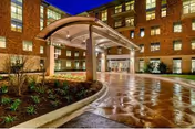 Entrance area of a multi-story brick building at night with a covered driveway and landscaped garden beds along the driveway.