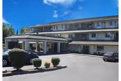 Exterior view of a three-story senior living facility named Horton Plaza with a covered entrance, several parked cars, and neatly trimmed bushes in the parking area under a clear blue sky.