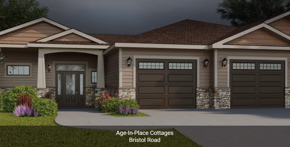 Exterior view of a single-story cottage with a front door, two garage doors, stone and wood siding, and landscaping with bushes and flowers under a cloudy sky.