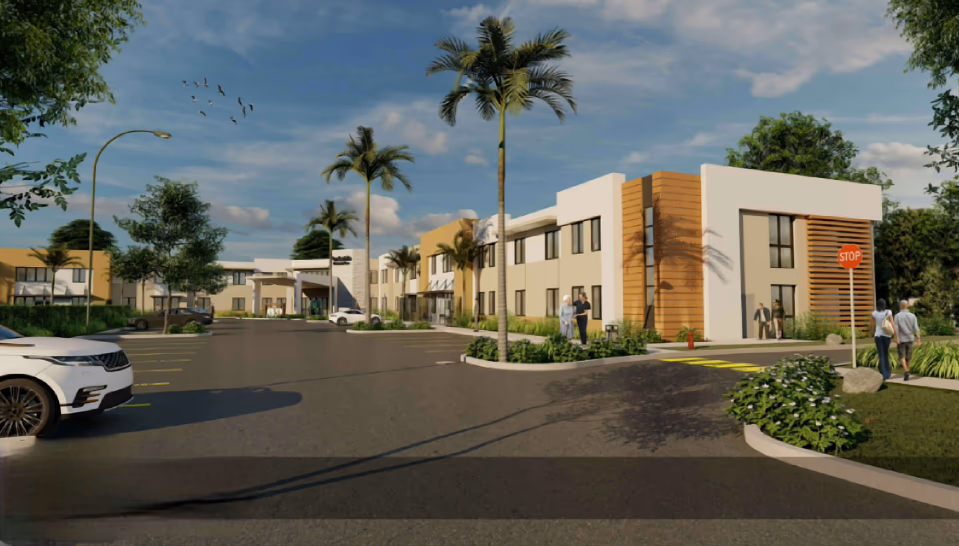 Exterior view of a modern two-story senior living facility with palm trees, parked cars, and people walking near the entrance under a partly cloudy sky.