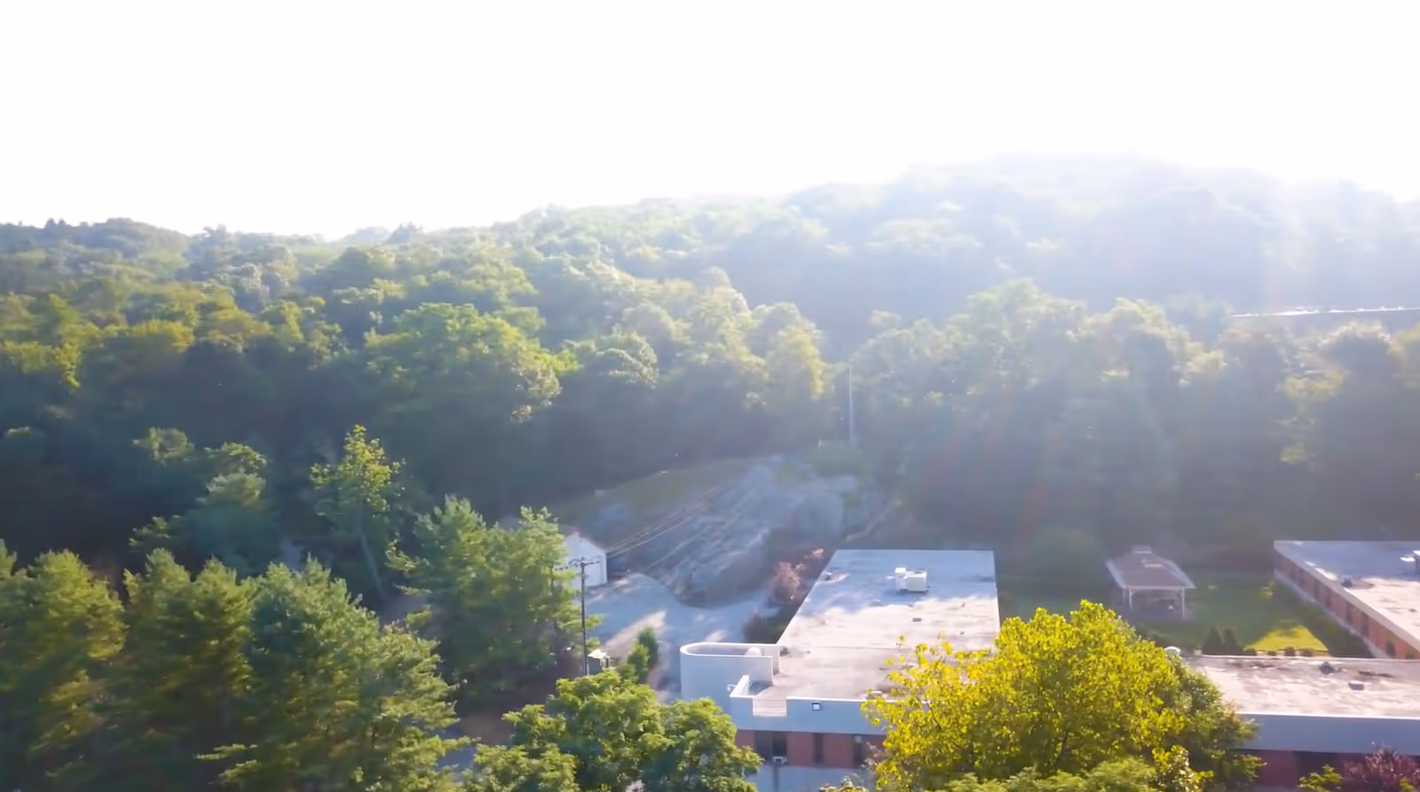 Aerial view of Salem Hills Rehabilitation and Healthcare facility surrounded by dense green trees and forested hills in the background under bright sunlight.