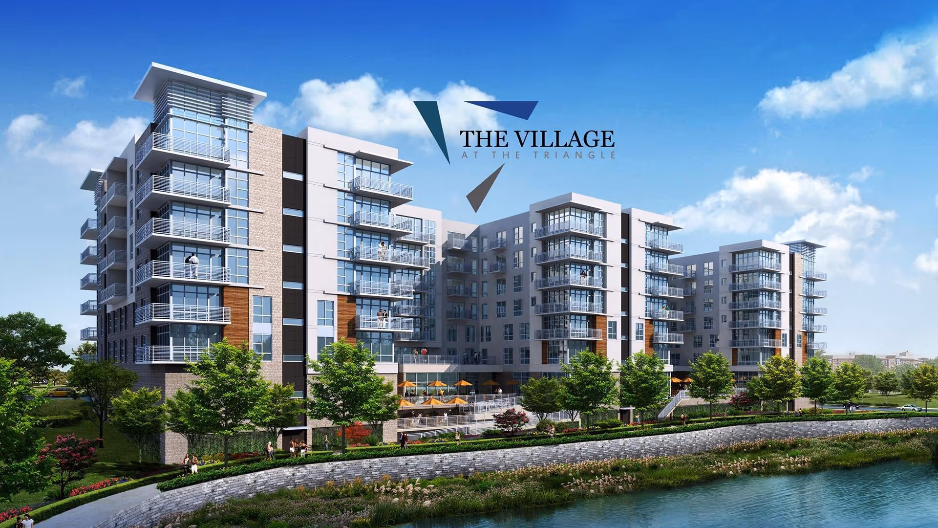 Exterior view of a modern multi-story senior living facility named The Village at The Triangle, featuring large glass windows, balconies, landscaped greenery, and a water body in the foreground under a blue sky with scattered clouds.