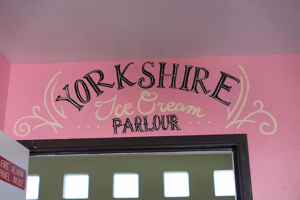 A pink wall with decorative text that reads 'YORKSHIRE Ice Cream PARLOUR' above a doorway. Part of a fire alarm panel sign is visible on the left side of the image.