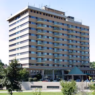 Exterior view of a multi-story retirement community building with balconies on each floor, surrounded by greenery and a clear sky.