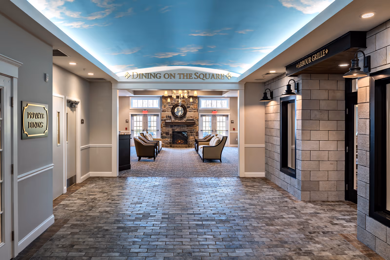 A hallway leading to a dining area with comfortable seating and a stone fireplace. The ceiling above the hallway is painted with a sky and clouds mural. Signs indicate 'Private Dining' on the left and 'Arbour Grille' on the right. Above the entrance to the dining area is a sign that reads 'Dining on the Square'.