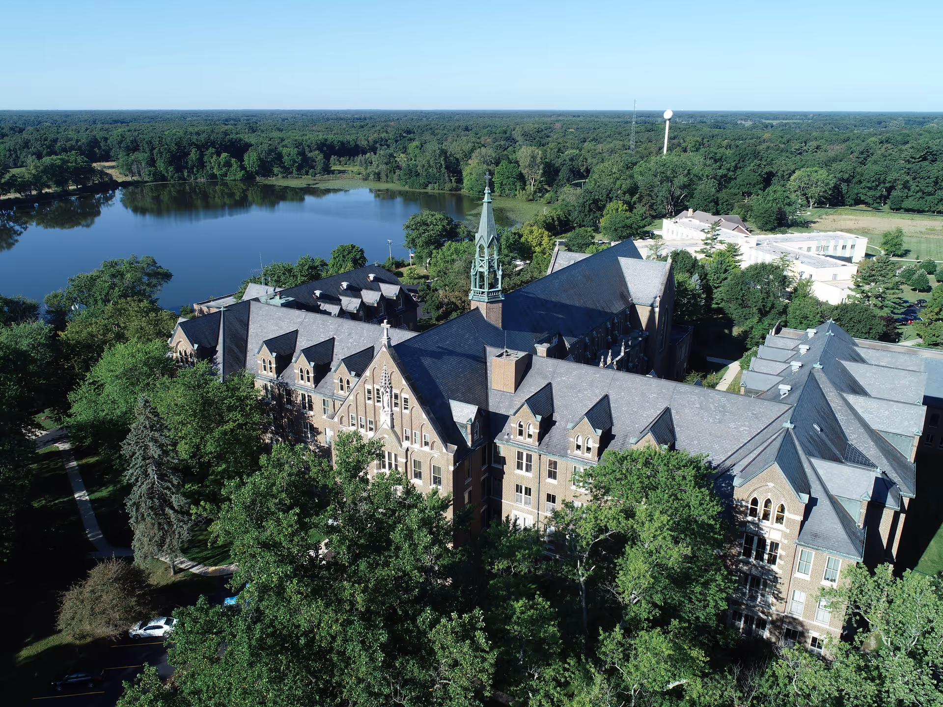 Aerial view of the Catherine Kasper Life Center building surrounded by trees with a large pond and forested area in the background under a clear blue sky.