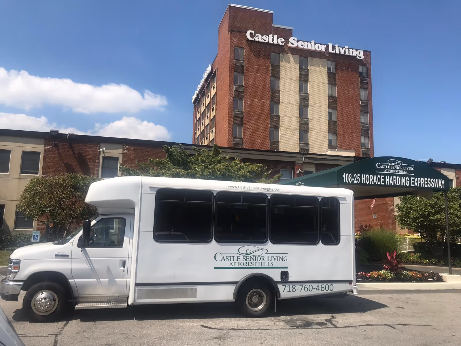 Exterior view of Castle Senior Living building with a white shuttle bus parked in front. The building is multi-story with a brick facade and the name 'Castle Senior Living' displayed at the top. There is a green awning at the entrance with the address 108-25 Horace Harding Expressway and the Castle Senior Living logo.