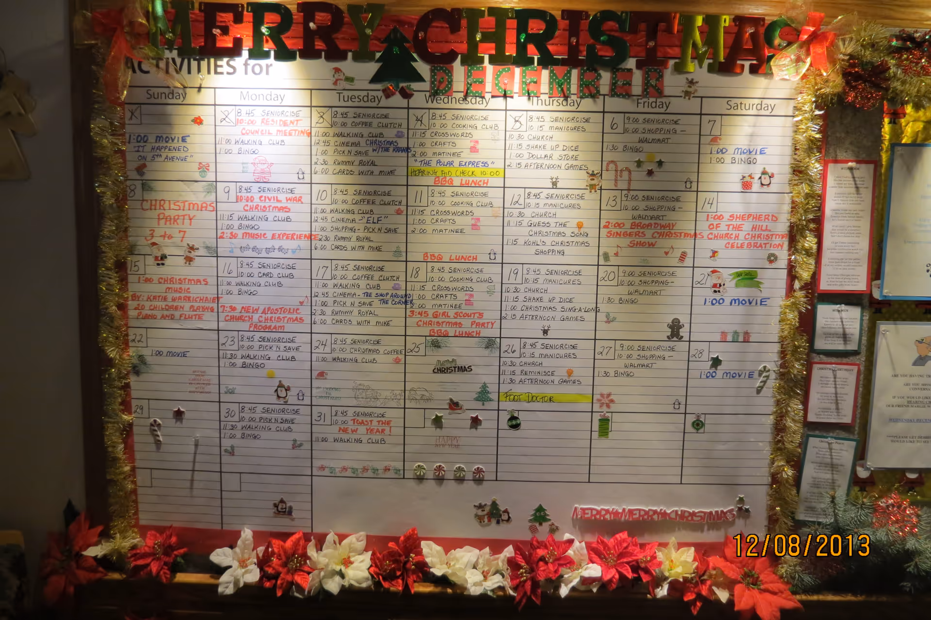 A decorated activity calendar board for December at Cecelia Place Assisted Living, featuring a variety of daily activities such as senior exercise, bingo, movie times, shopping trips, and holiday events. The board is adorned with Christmas decorations including tinsel, poinsettias, and festive stickers. The date 12/08/2013 is visible in the bottom right corner.