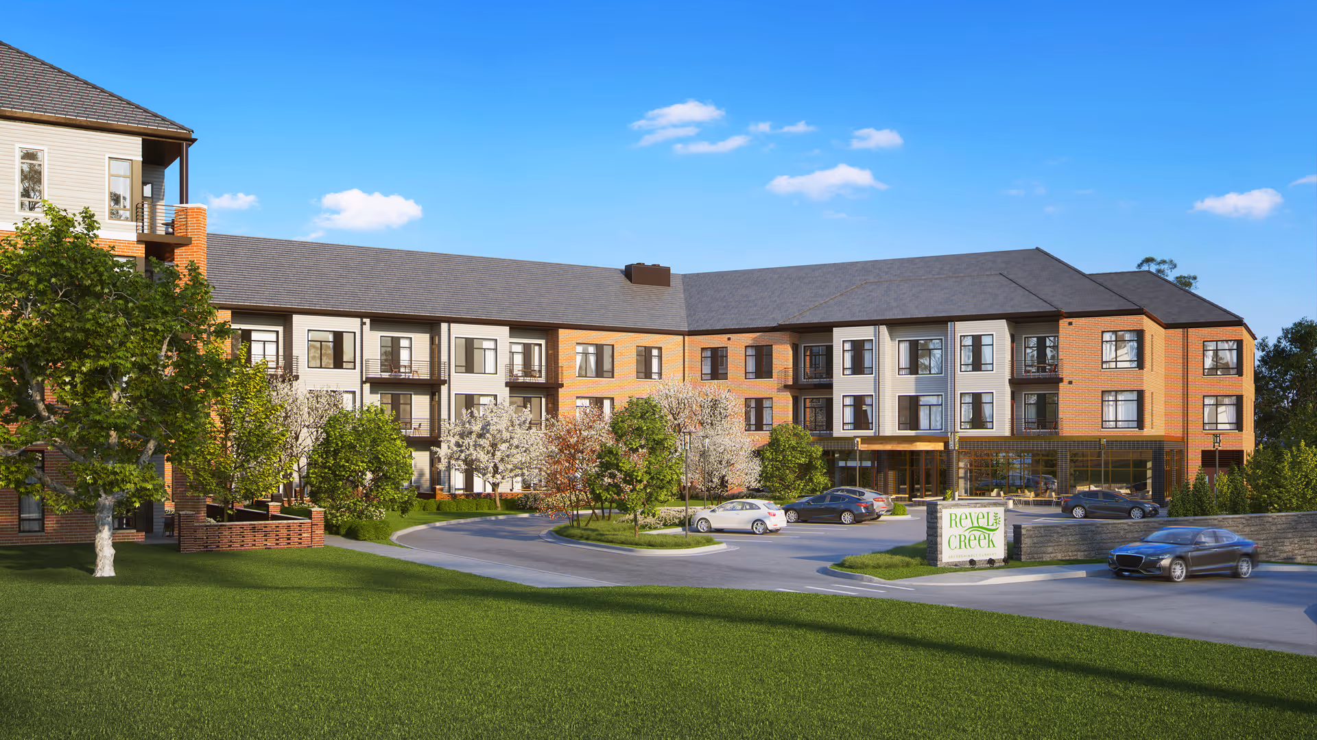 Exterior view of a modern three-story senior living facility with a combination of brick and light-colored siding. The building has multiple windows and balconies, surrounded by green lawns, trees, and a driveway with parked cars under a clear blue sky.