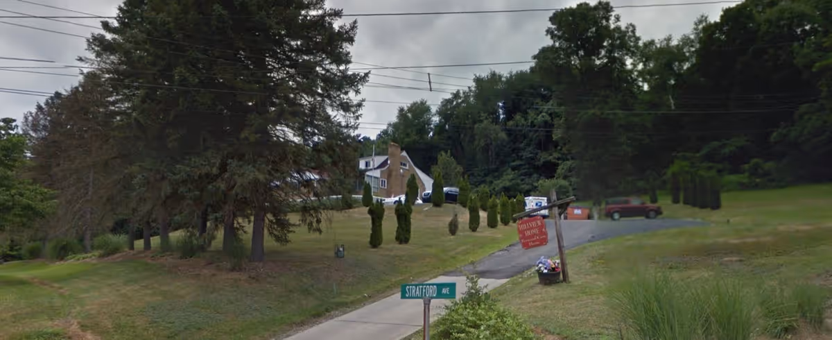 Exterior view of Hillview Home with a sign, surrounded by greenery and trees, and a driveway leading up to the building.
