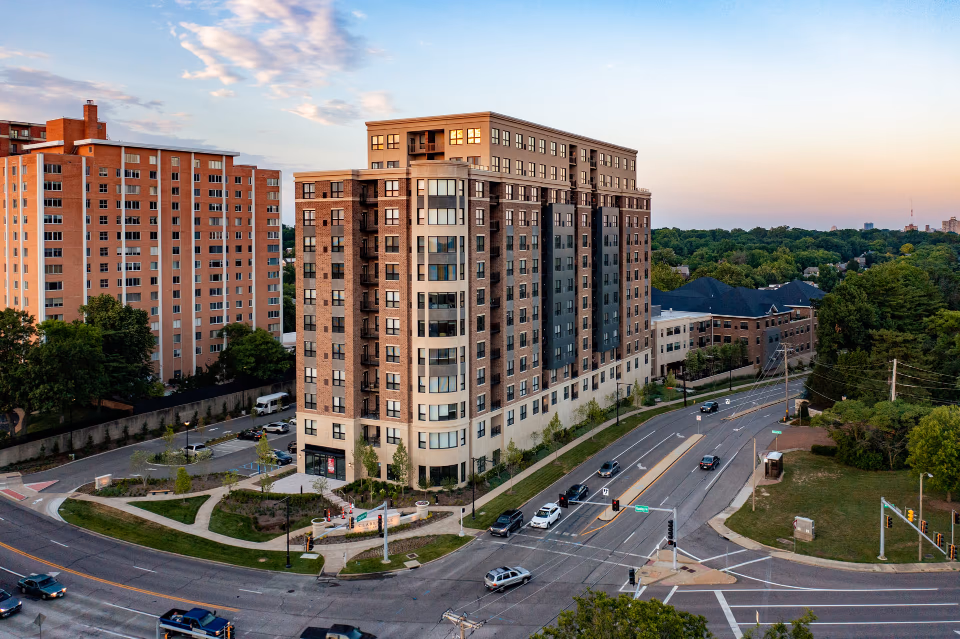 Aerial view of a multi-story residential building named Clarendale Clayton, surrounded by roads, greenery, and other buildings during sunset.