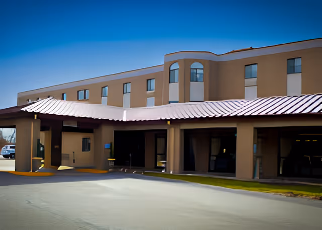 Exterior front view of a multi-story senior living facility building with a covered entrance and several windows under a clear blue sky.