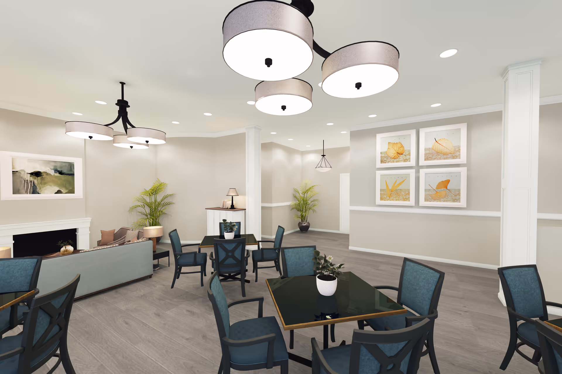 A spacious and well-lit common area with several tables and chairs arranged for seating. The room features modern light fixtures on the ceiling, framed artwork on the walls, potted plants, and a cozy seating area with a sofa and armchairs near a fireplace.