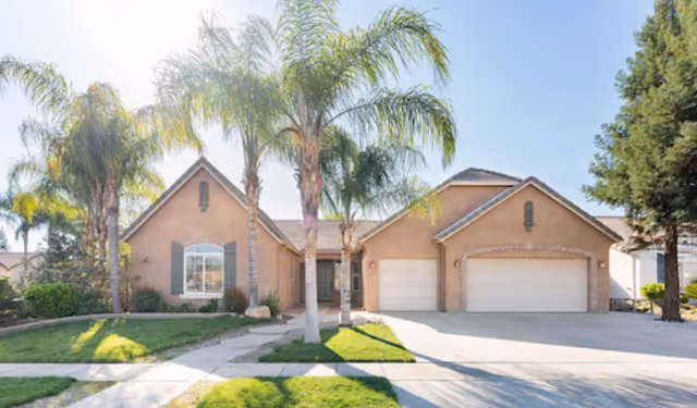 Front exterior view of a single-story residential building with a three-car garage, palm trees, and a well-maintained lawn under a clear blue sky.