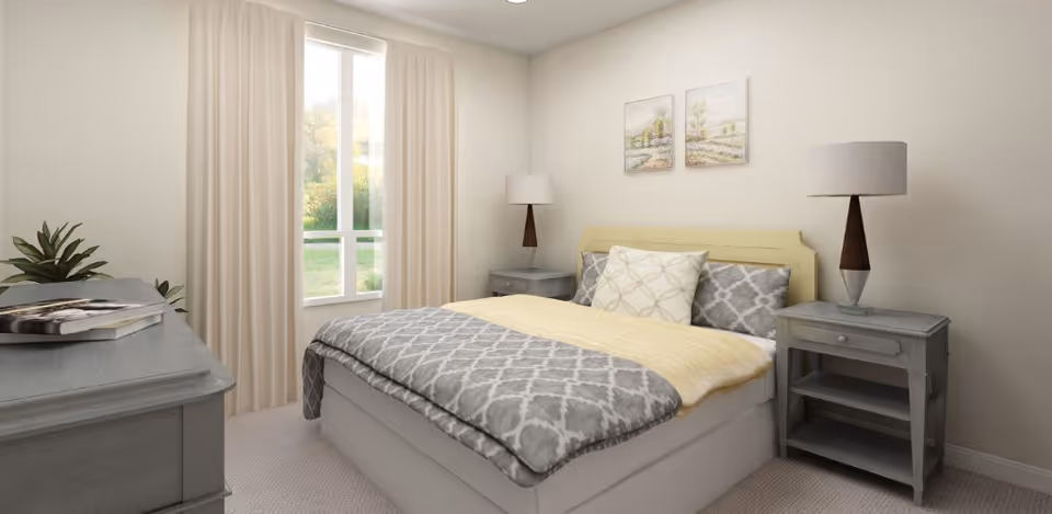 A cozy bedroom with a bed featuring gray and white patterned bedding and a yellow blanket. There are two matching gray nightstands on either side of the bed, each with a lamp. A window with beige curtains lets in natural light, and two framed landscape paintings hang above the bed. A gray dresser with a book and a plant on top is visible on the left side of the room.