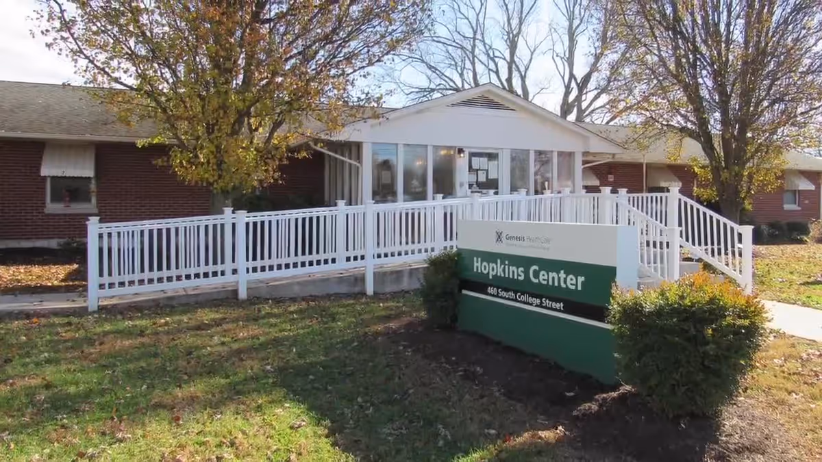 Exterior view of Hopkins Center, a single-story brick building with a white entrance ramp and railing. There are trees with autumn leaves and a green and white sign in front that reads 'Hopkins Center, 460 South College Street.'