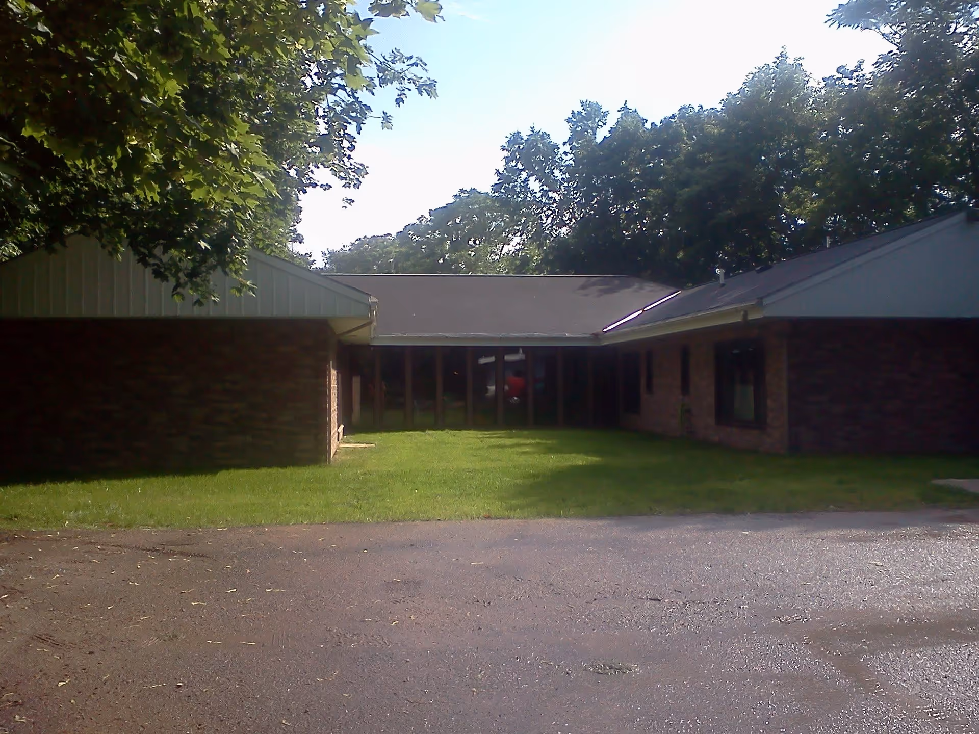 Exterior view of a single-story brick building with a pitched roof, surrounded by green grass and trees under a clear sky.
