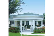 Exterior view of a white building with a covered entrance supported by columns, surrounded by green grass and landscaping under a clear blue sky.