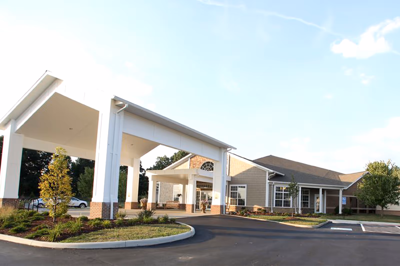 Exterior view of Danbury Massillon facility showing the entrance with a large covered drop-off area, landscaped greenery, and a parking lot under a clear sky.