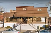 Exterior view of a two-story brown building with a white base and stairs leading up to the entrance. There are some bushes and parked cars in front of the building. The sign on the building reads 'Wavecrest HFA'.
