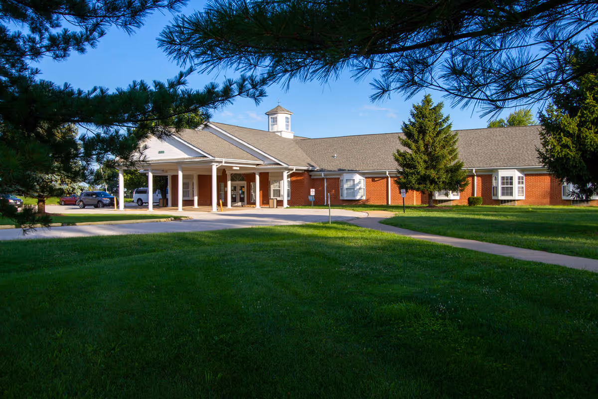 Front exterior view of Oakwood Estates Nursing & Rehab building with a covered entrance, surrounded by green grass and trees under a clear blue sky.