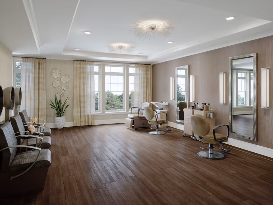 A bright and spacious hair salon area with large windows letting in natural light. The room features wooden flooring, three salon chairs in front of large mirrors with wall-mounted lights, and a row of waiting chairs with armrests on the left side. There is a potted plant and decorative wall art near the windows.