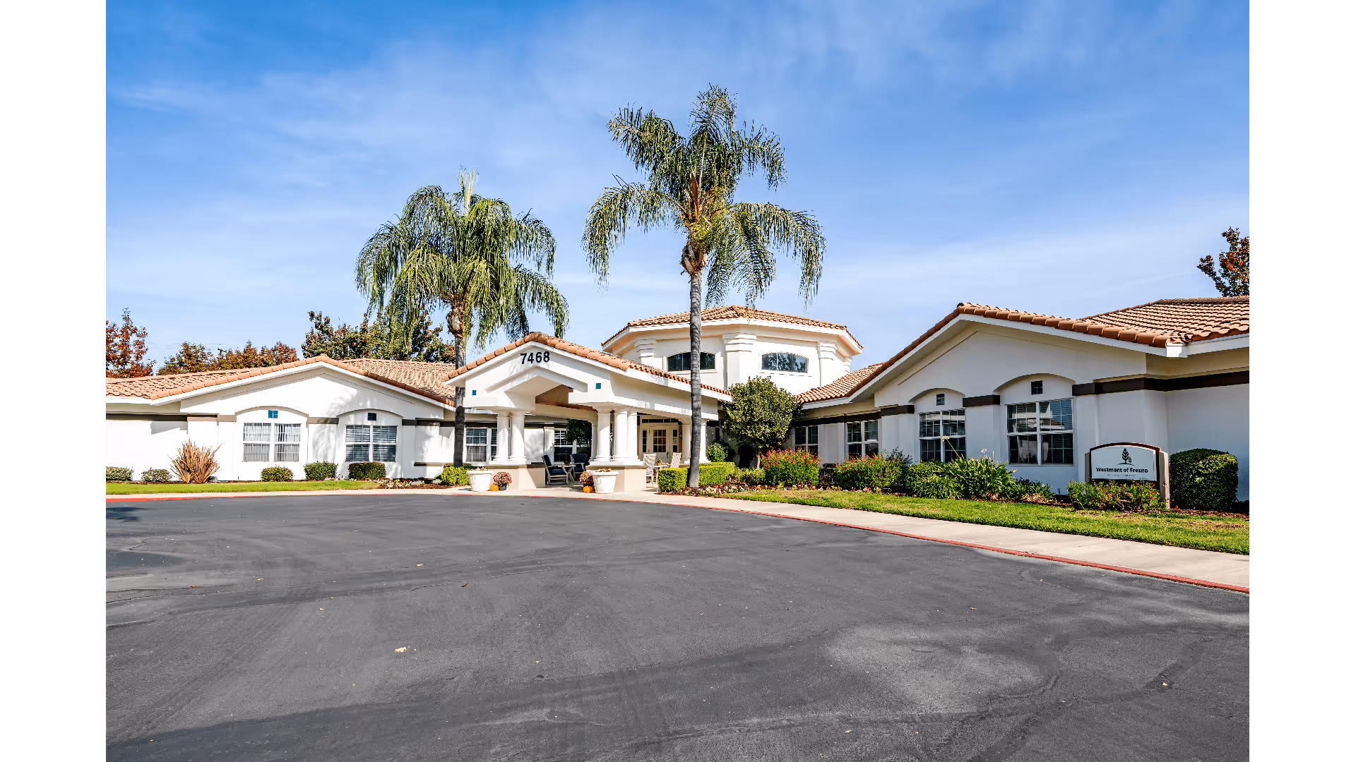 Exterior view of Westmont of Fresno senior living facility with a circular driveway, palm trees, and a clear blue sky.