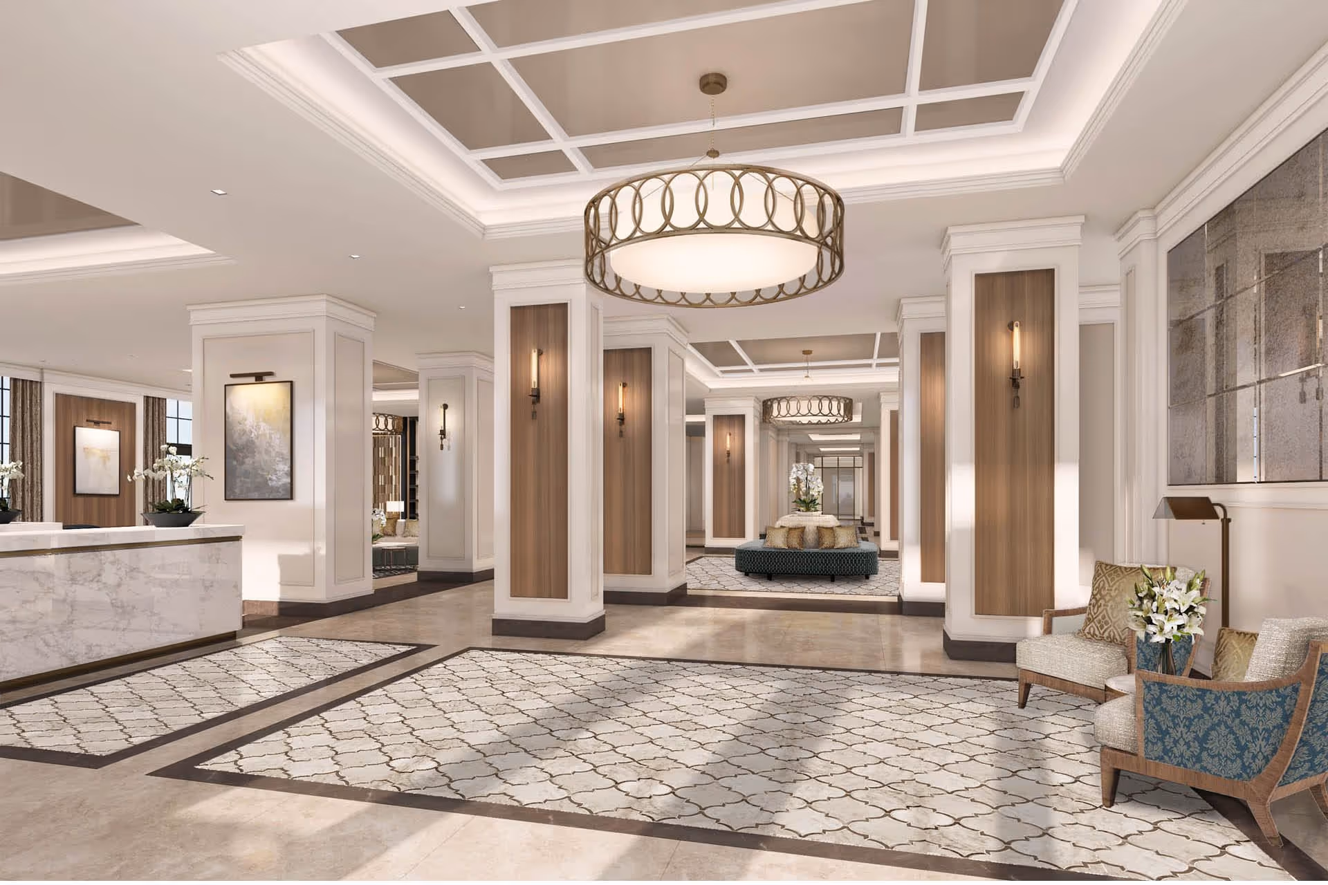 A spacious and elegant lobby area with a marble reception desk on the left, decorative rugs on the floor, multiple white columns with wooden panel accents, modern wall sconces, and large circular chandeliers hanging from a coffered ceiling. There are comfortable chairs with cushions and a small table with flowers on the right side, and a round seating area with pillows and flowers in the background.