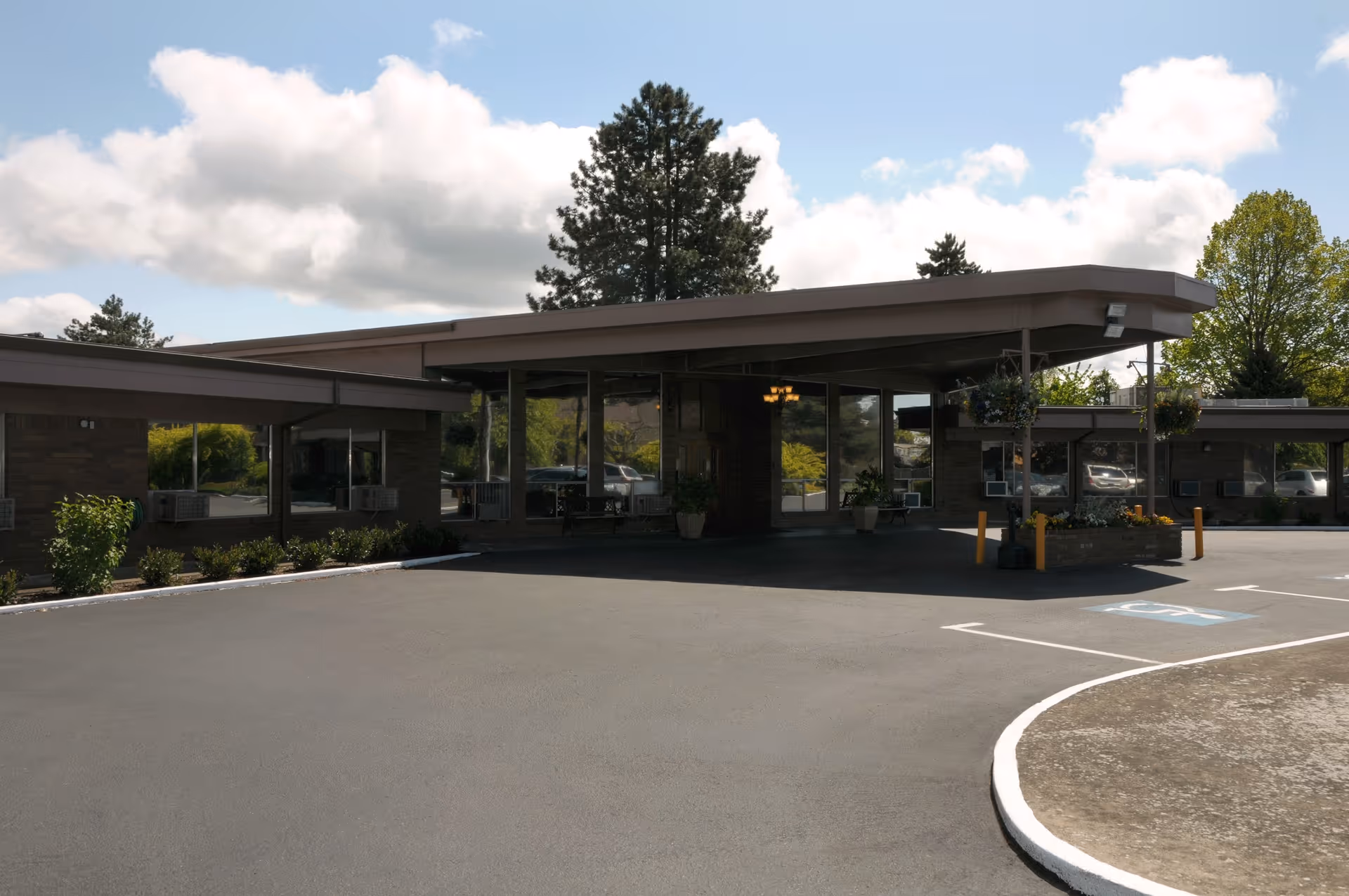Exterior view of the Life Care Center of McMinnville building entrance with a covered driveway, surrounded by trees and a partly cloudy sky.