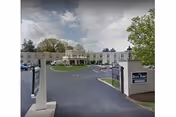 Entrance driveway leading to a two-story beige building with a circular driveway and a covered entrance. There are trees and a lawn area around the building. A sign near the entrance reads 'Bryn Mawr Extended Care Center.'
