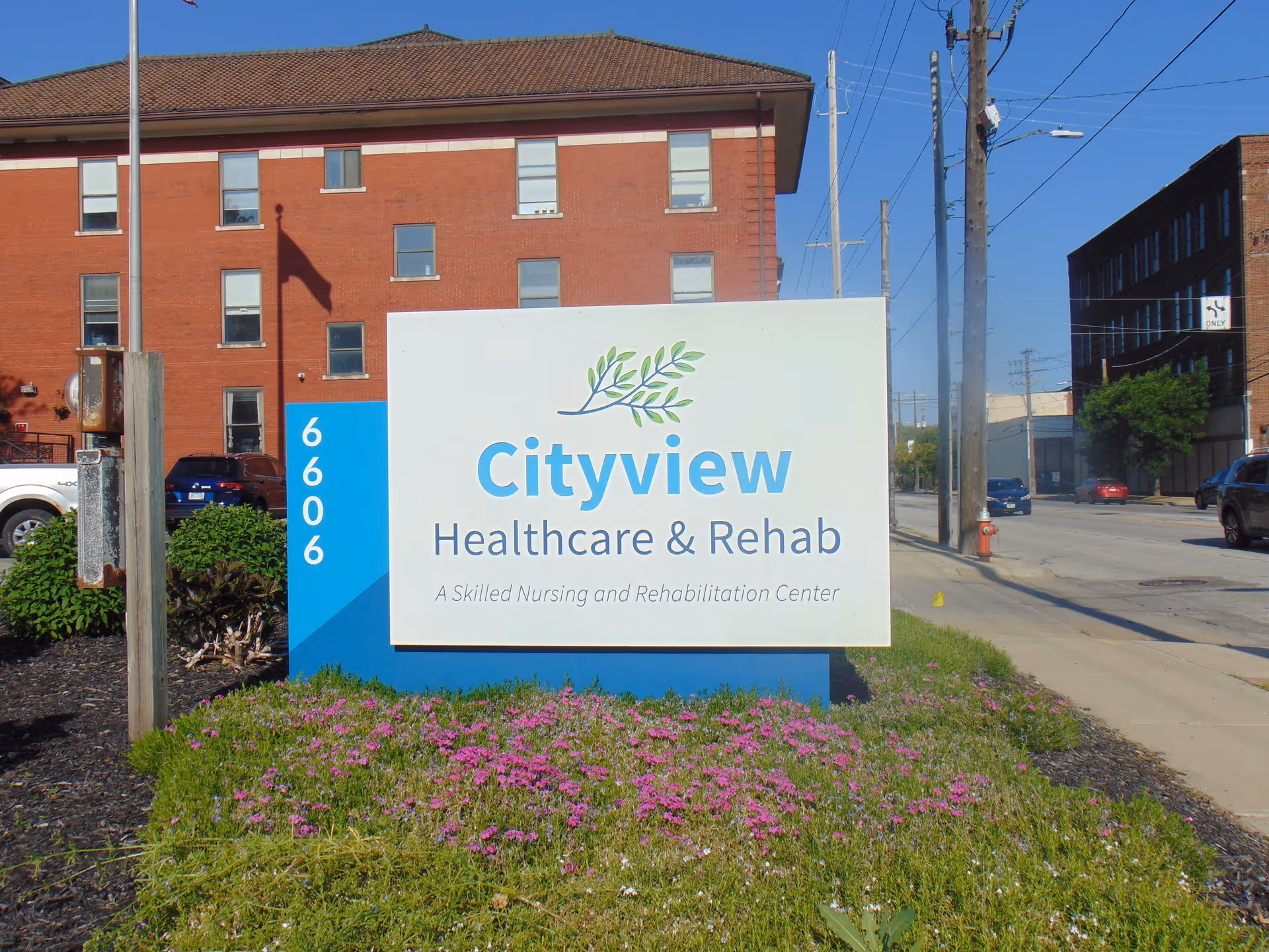 Outdoor view of a sign for Cityview Healthcare & Rehabilitation, a skilled nursing and rehabilitation center, with a brick building and street in the background.