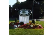 Outdoor view of a landscaped area with a white wooden signpost displaying the name 'White Oaks Rehabilitation and Nursing Center' surrounded by flowers and greenery.