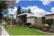 Exterior view of Garden Park Care Center building with a well-maintained lawn, trimmed bushes, and a sign displaying the facility's name under a partly cloudy sky.