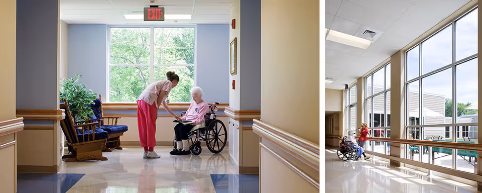 Two images showing an elderly woman in a wheelchair interacting with a caregiver in a nursing facility. The first image shows the caregiver bending down to talk to the elderly woman in a hallway with large windows and wooden rocking chairs. The second image shows the elderly woman and caregiver near large floor-to-ceiling windows overlooking an outdoor patio area.