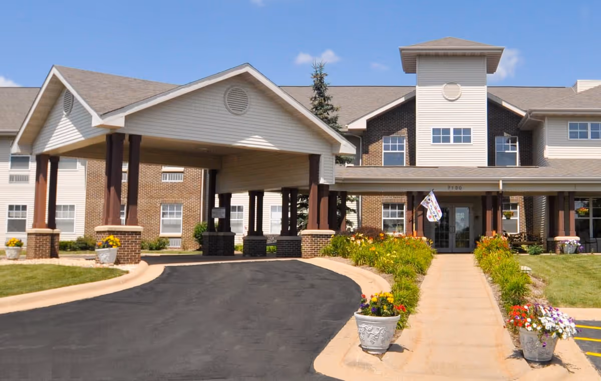 Front exterior view of Charter Senior Living of Rockford building with a covered entrance, flower pots along the walkway, and a clear blue sky.