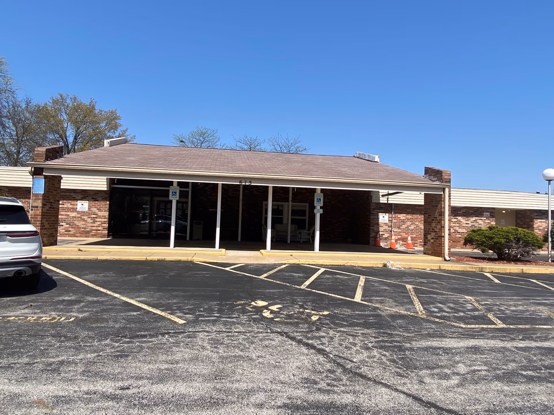 Exterior front view of Rancho Rehab and Healthcare Center building with a covered entrance, brick walls, and a parking lot with marked handicap parking spaces under a clear blue sky.