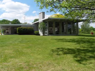 A single-story building with large windows and a flat roof surrounded by a well-maintained green lawn and trees under a partly cloudy sky.