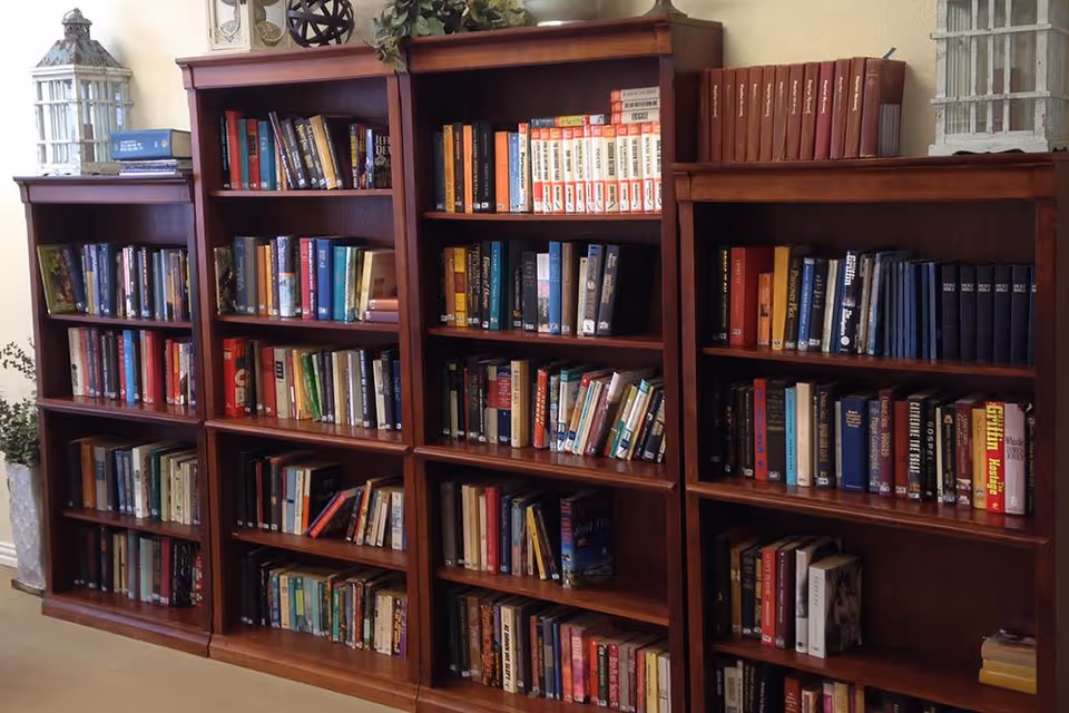 A set of four wooden bookshelves filled with various books arranged neatly. Decorative items, including two white lanterns and a small plant, are placed on top of the bookshelves. The setting appears to be a quiet indoor reading or library area.