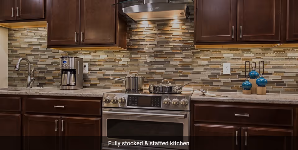 Modern kitchen with dark wooden cabinets, a stainless steel stove with pots on it, a coffee maker, a sink with a faucet, and a tiled backsplash with under-cabinet lighting.