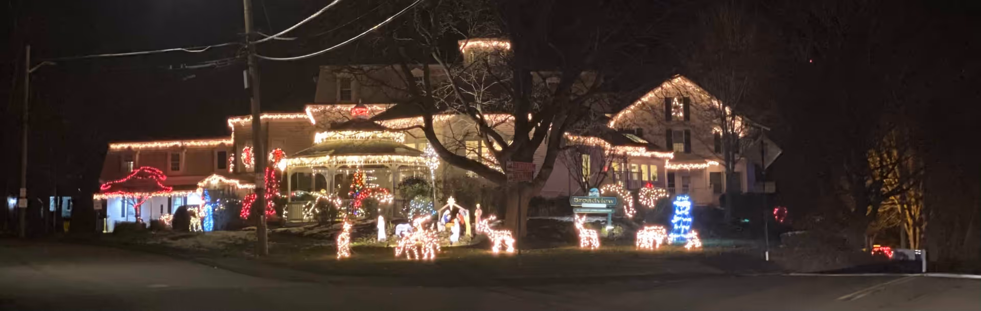 A large building decorated with Christmas lights at night, featuring illuminated reindeer, candy canes, and other holiday decorations on the lawn and around the porch area.