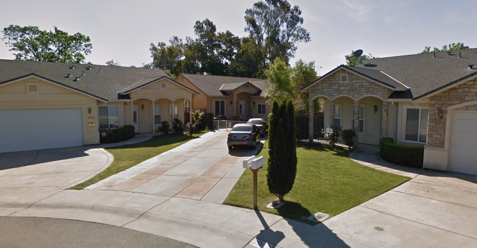 View of a residential facility with single-story homes featuring garages, driveways, and small front lawns with trees and shrubs under a clear sky.
