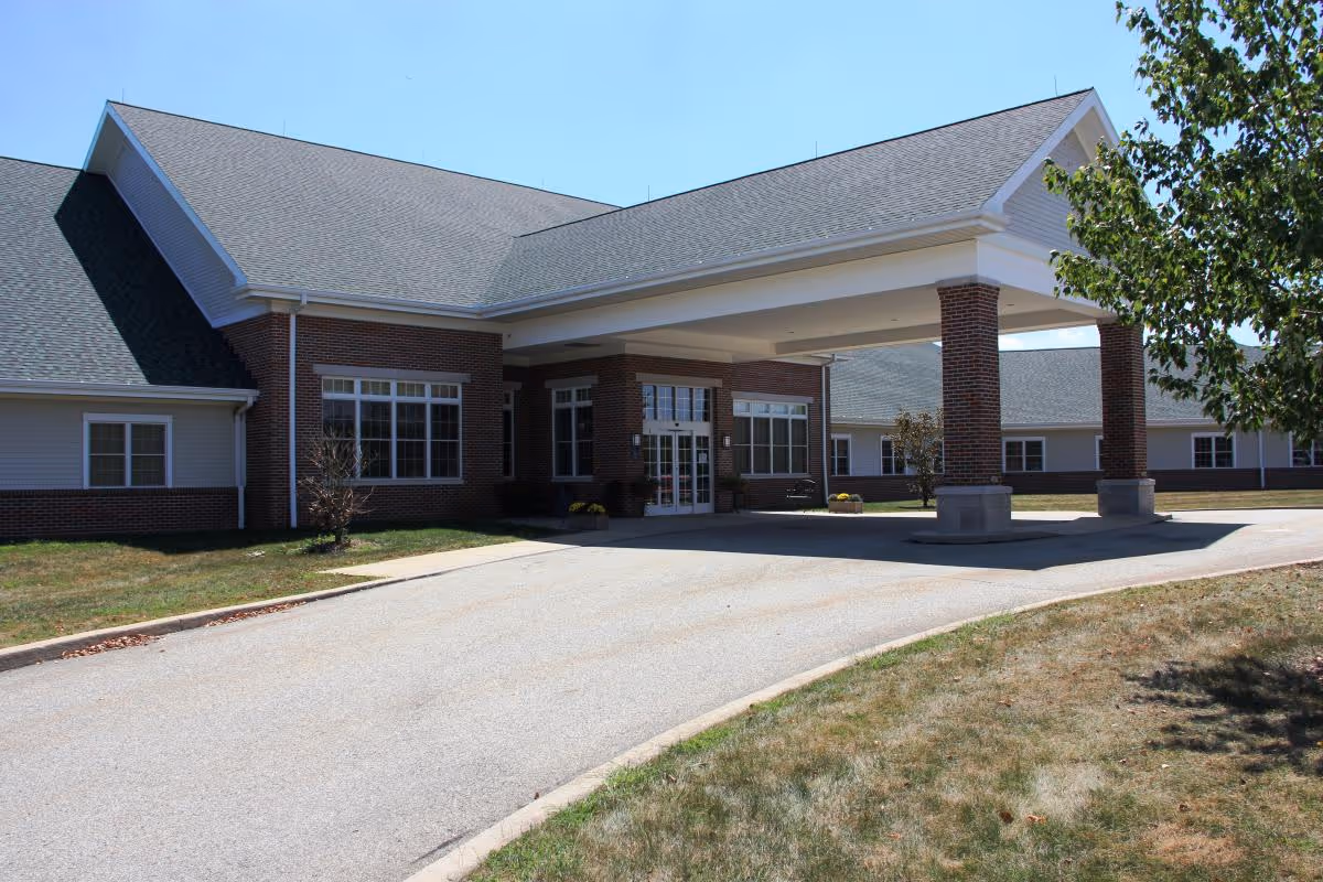 Exterior view of Bethlen Home Skilled Nursing and Rehabilitation building with a covered entrance supported by brick columns, surrounded by grass and a tree on the right side under a clear blue sky.