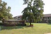 Exterior view of Spring River Christian Village facility with a large green lawn, trees, and a sign displaying the facility name in front of a two-story building under a clear sky.
