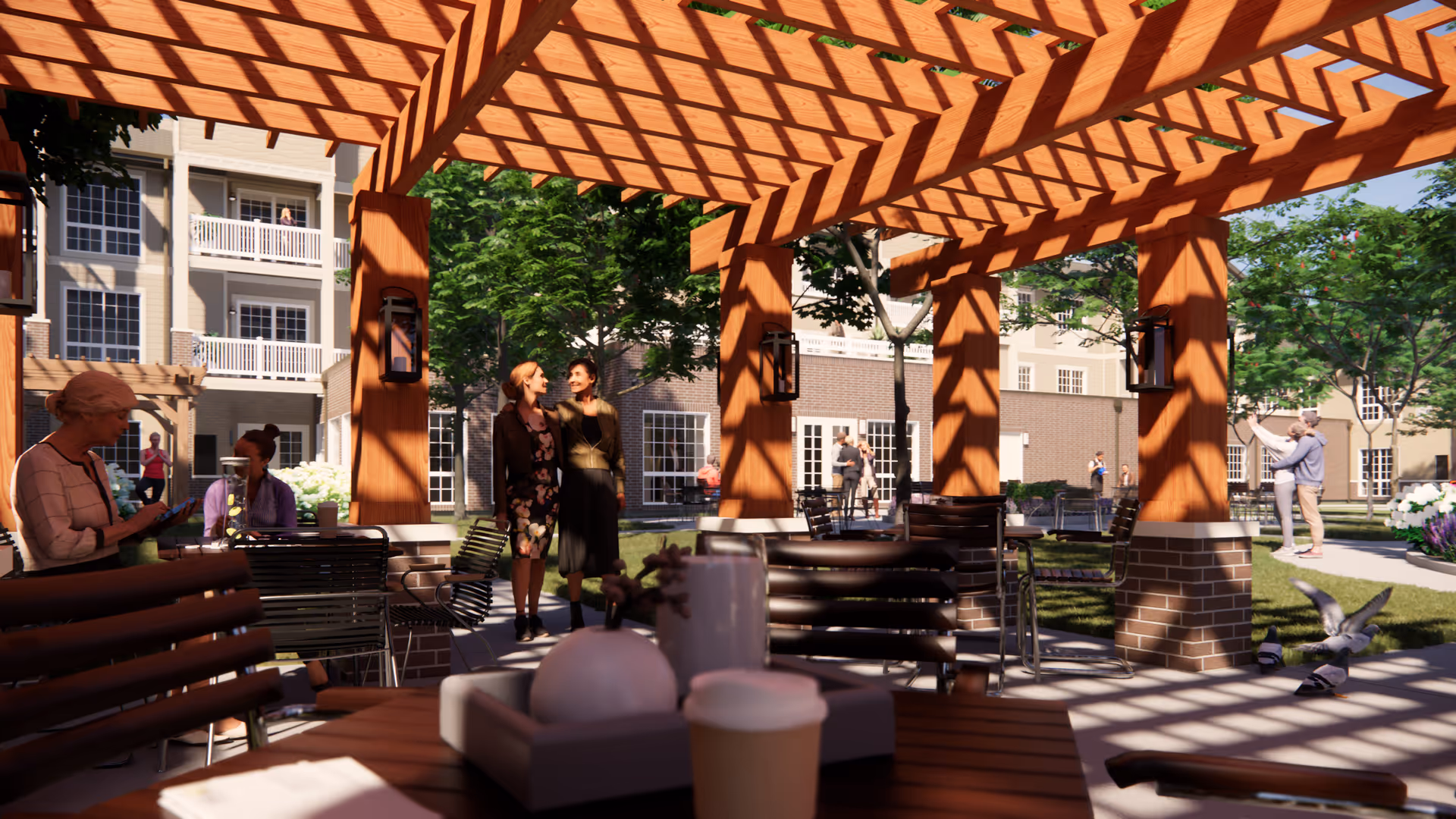 Outdoor seating area under a wooden pergola with tables and chairs. Several people are seen socializing and walking around in a garden-like courtyard with trees and a multi-story building in the background.