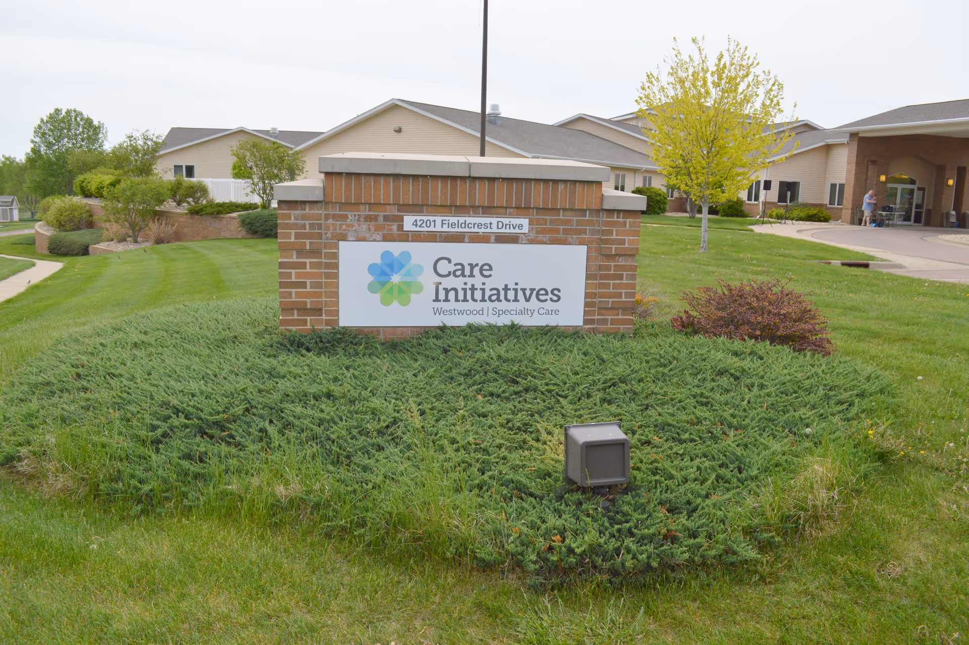 Brick sign for Care Initiatives Westwood Specialty Care at 4201 Fieldcrest Drive surrounded by green grass and shrubs with the facility building and entrance visible in the background.
