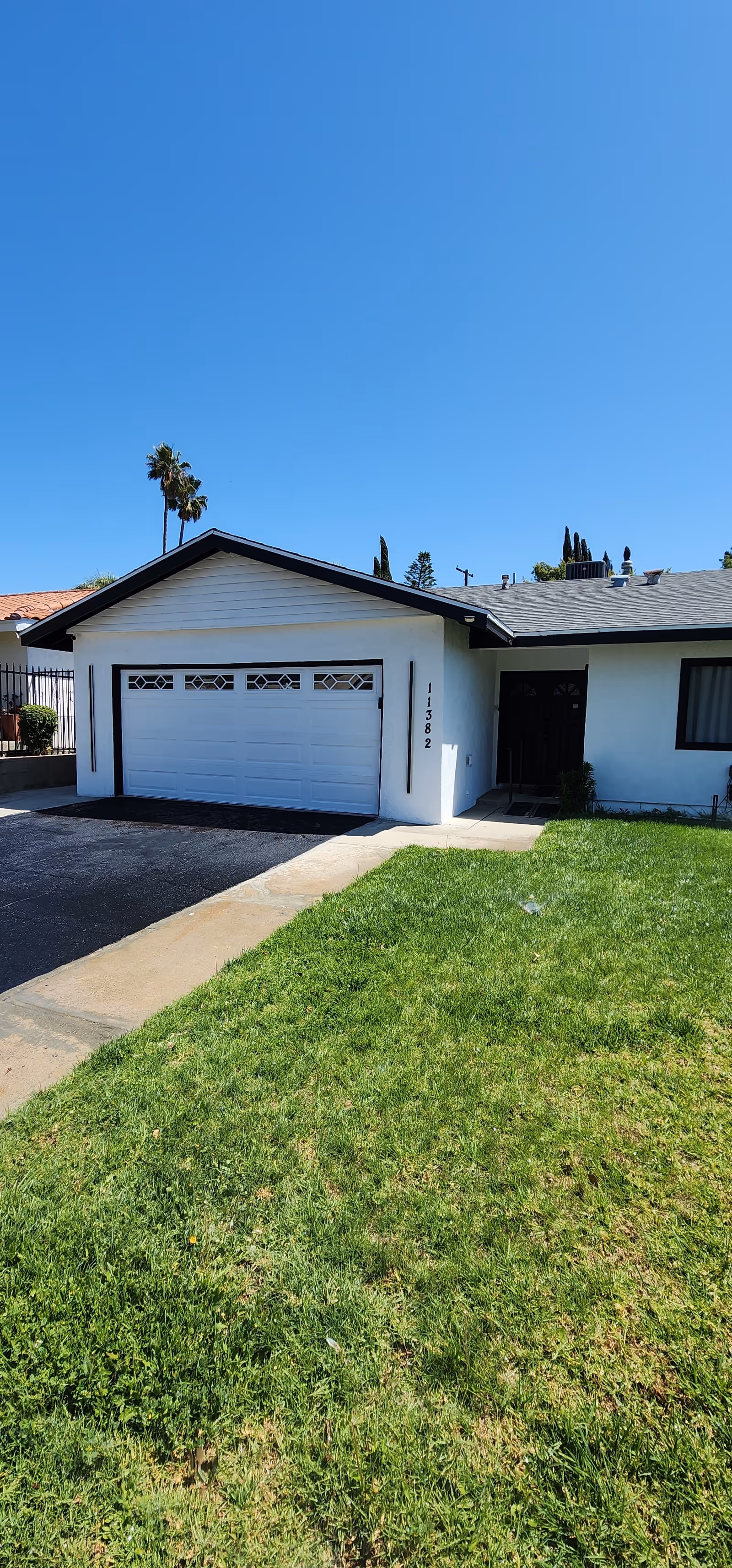 Single-story residential building with a white garage door and a green lawn in front under a clear blue sky.