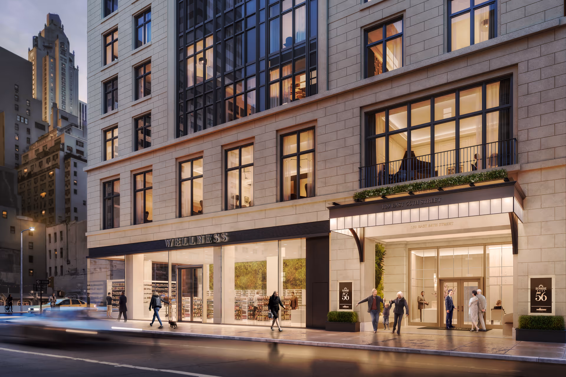 Exterior view of a modern multi-story building at dusk with large windows and a well-lit entrance. People are walking on the sidewalk in front of the building, which has signs reading 'Sunrise at East 56th' and 'Wellness'. The street and surrounding city buildings are visible.