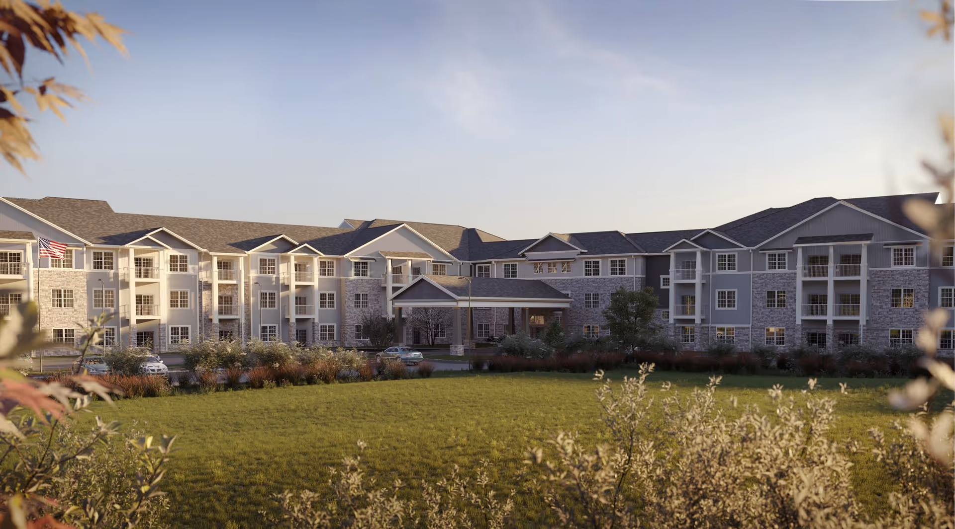 Exterior view of a large senior living facility building with multiple floors, balconies, and a covered entrance. The building is surrounded by landscaped greenery and a well-maintained lawn under a clear sky.