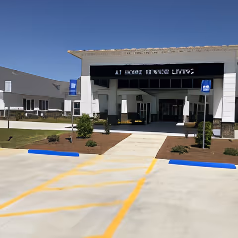 Front exterior view of At Home Senior Living of Cochran building with a covered entrance, blue sky, and a parking area with yellow and blue markings in front.